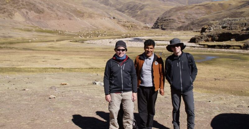 a group of smiling men trekking in the Peruvian Andes with Alpaca grazing in the distance