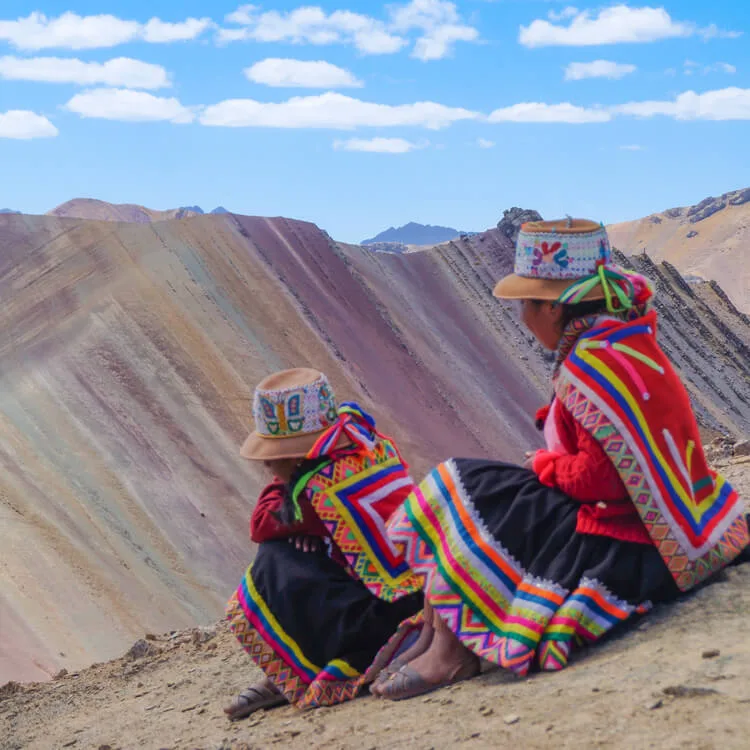 Two people wearing local traditional clothes and sitting in front of the Rainbow Mountain 