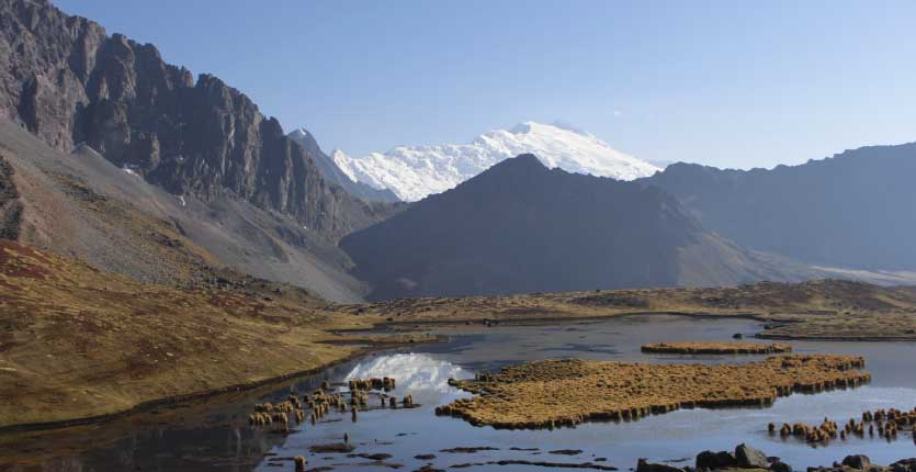 The Ausangate peak is seen from behind other mountains that cover a lake.