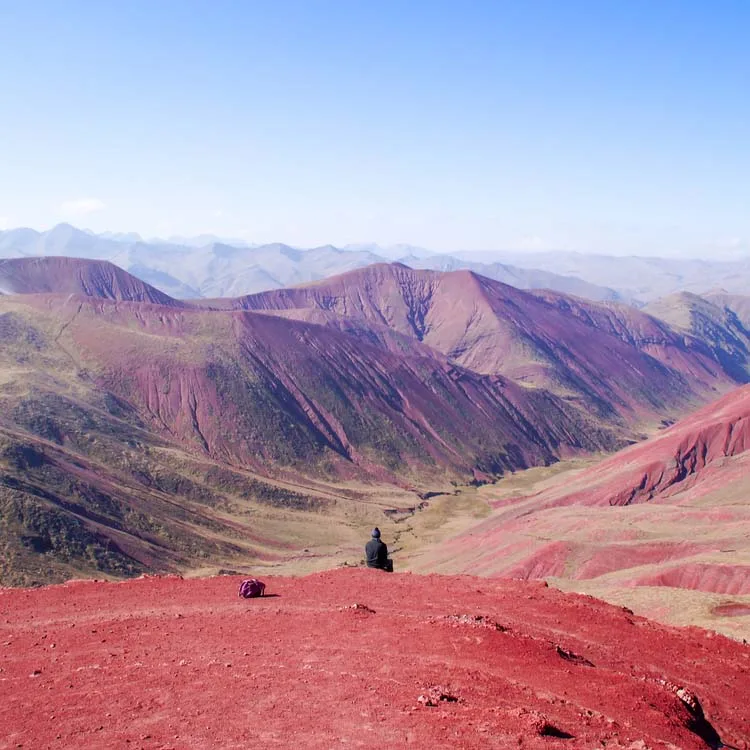  A lone traveler sits on the striking red terrain of Peru’s Red Valley, gazing into the sweeping layers of colored hills and deep valleys.
