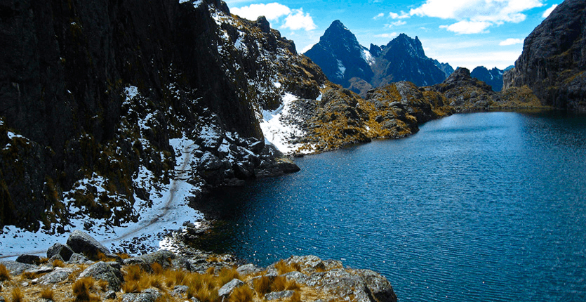A blue lake between several mountains that have fallen snow on them.