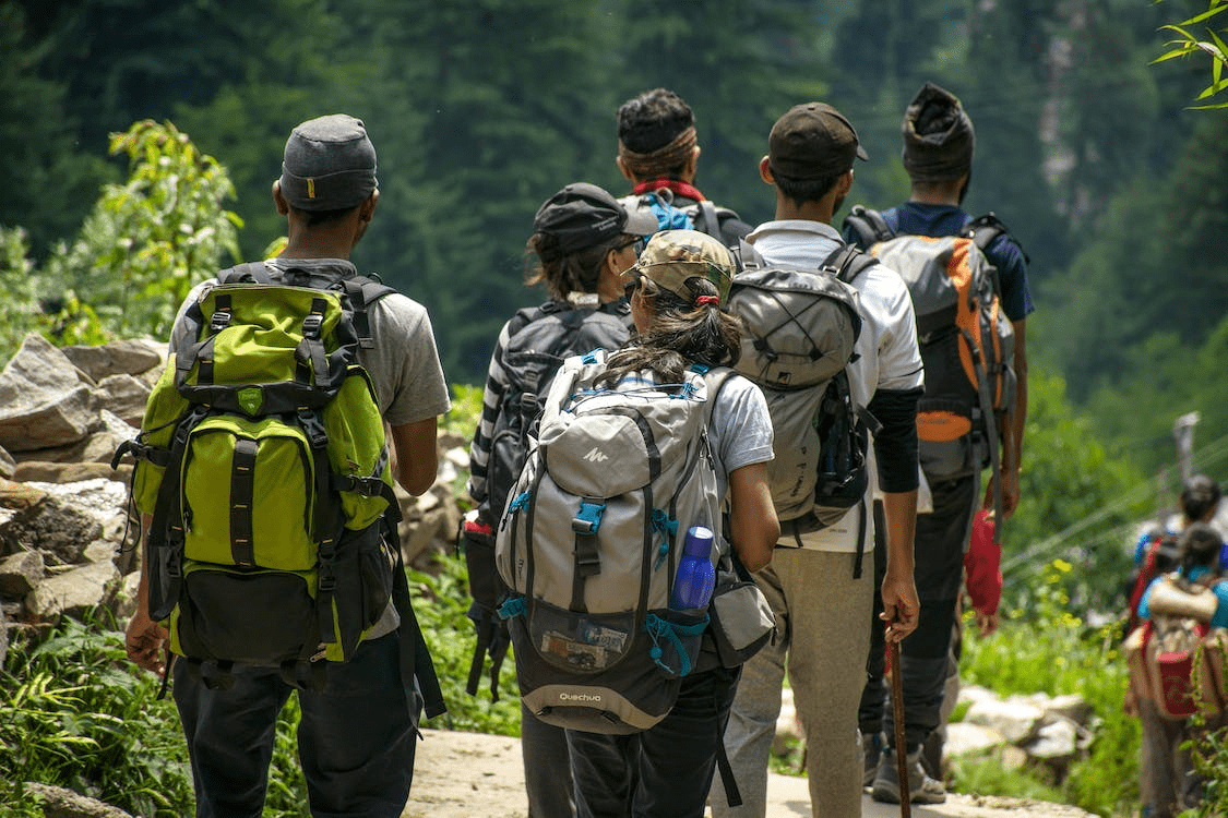 A group of people wearing bags on their shoulders and hiking through a mountainous area.