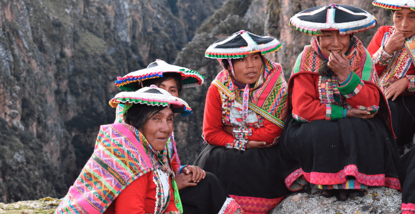 A group of native Peruvian women is wearing traditional attires while sitting together at the edge of a cliff.