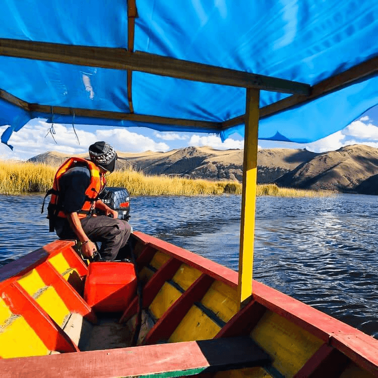 Local guide navigating a colorful boat across one of the Four with Andean mountains in the background.