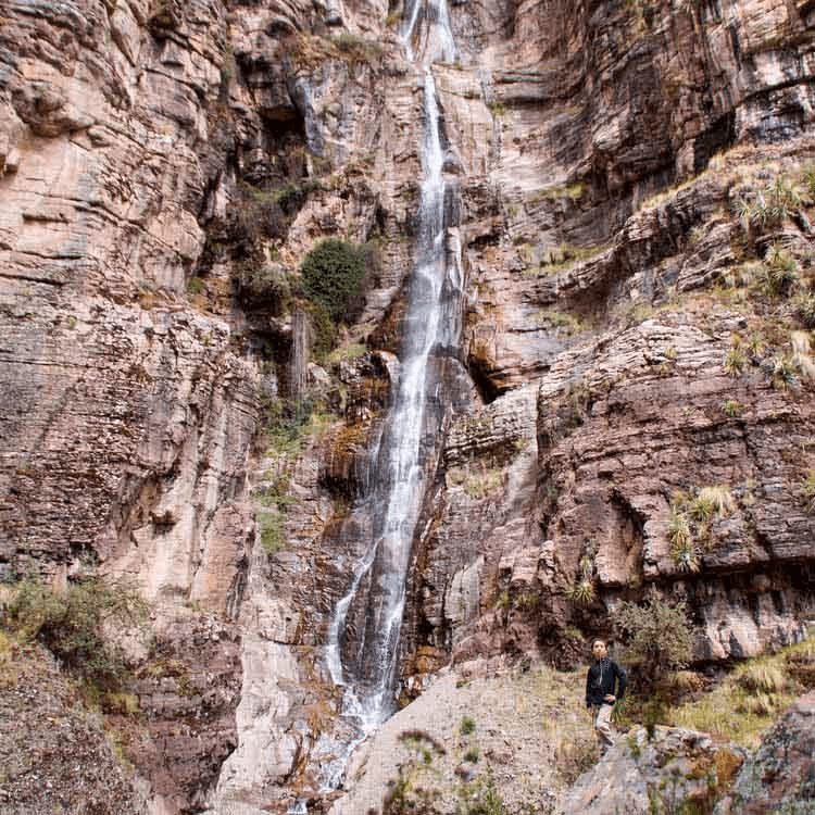A person posing for a photo with a mountain and waterfall in the background.