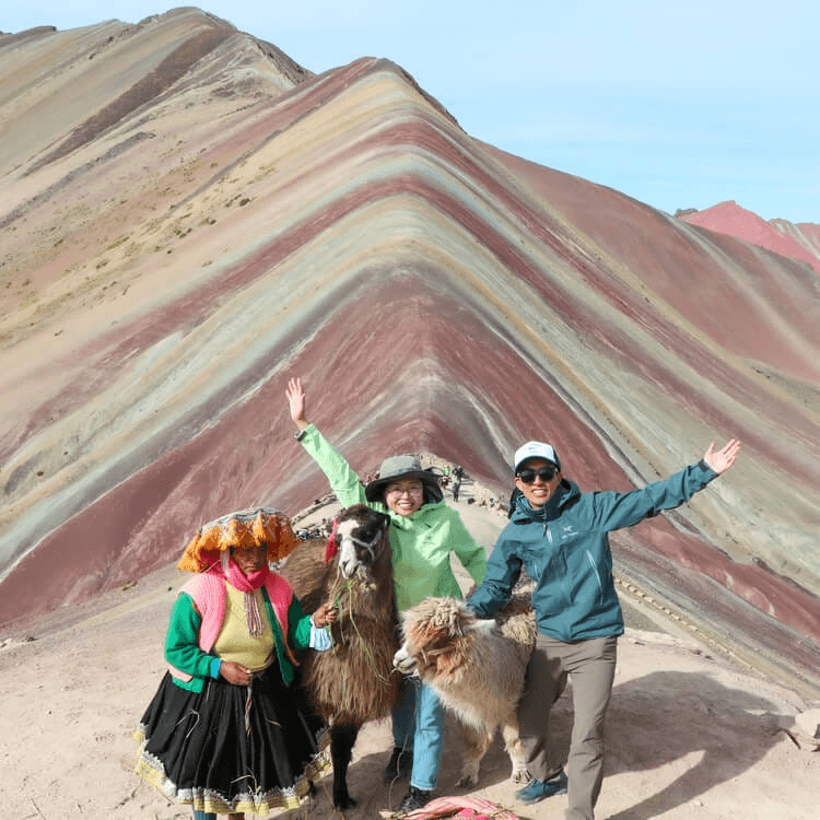 Two tourists posing for a photo with a local and llamas at Rainbow Mountain.
