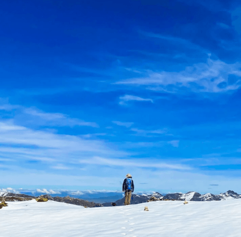 A lone hiker stands on a vast snow-covered plateau beneath a brilliant blue sky during the Ausangate Trek in the Peruvian Andes.
