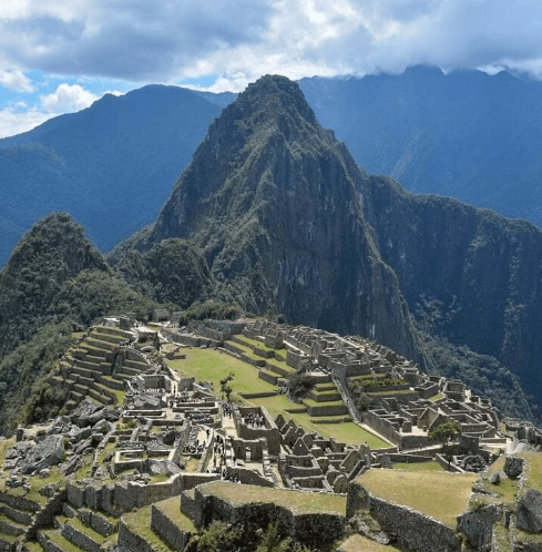 machu picchu day trip cusco A panoramic view of the ancient Incan citadel of Machu Picchu, perched on a mountain ridge and surrounded by lush, misty green peaks in Peru.