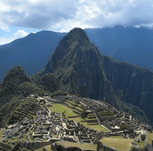 A sweeping view of Machu Picchu’s ancient stone ruins nestled among green terraces and surrounded by steep, lush mountains under a clear Andean sky.