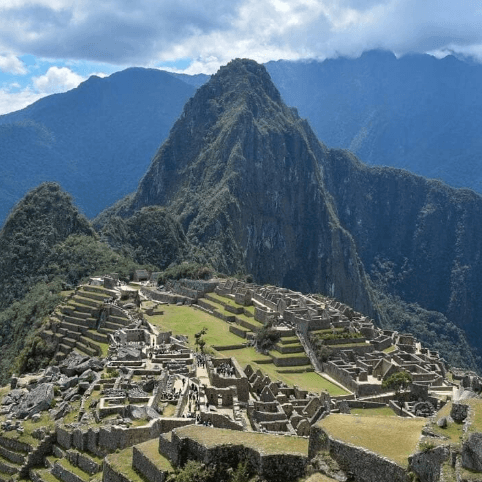 Elevated view of Machu Picchu’s stone ruins and green terraces nestled among the Andes, with steep mountain peaks towering in the background under a clear sky.
