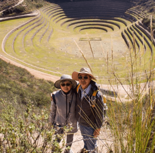 Two tourists smiling for the camera while hiking a dirt path through grassy highlands in the Sacred Valley.