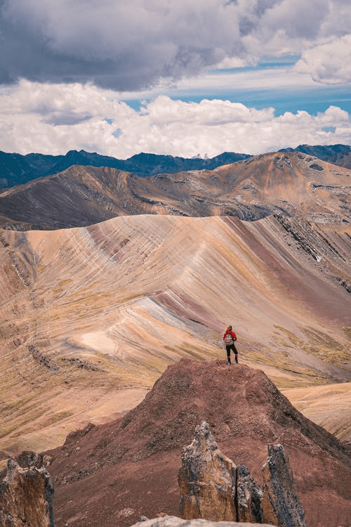 Solo hiker above striped ridges at Vinicunca at the Rainbow Mountain in Cusco, Peru.