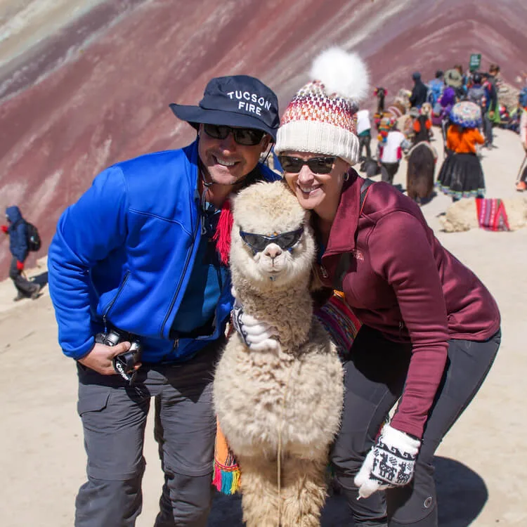 2 tourists posing with a Llama  