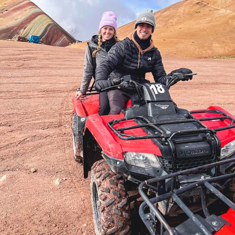 a couple wearing warm clothes sitting on a red ATV for the tour of Rainbow Mountain
