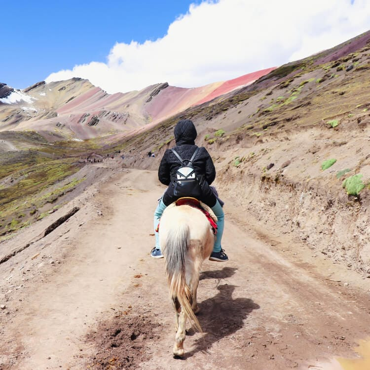 a person sitting on a horse trekking up the Rainbow Mountain