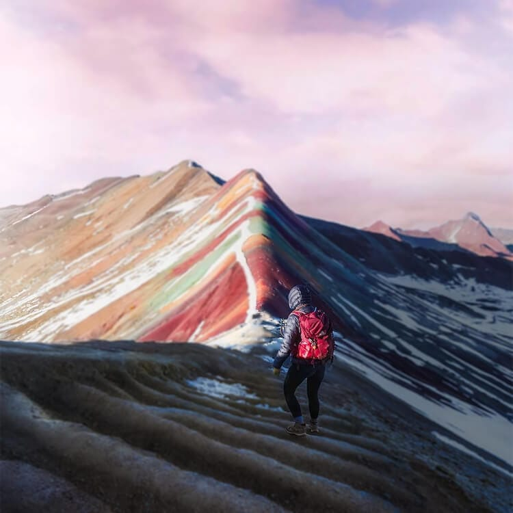 A lone hiker with a red backpack standing on the ridge of Rainbow Mountain.