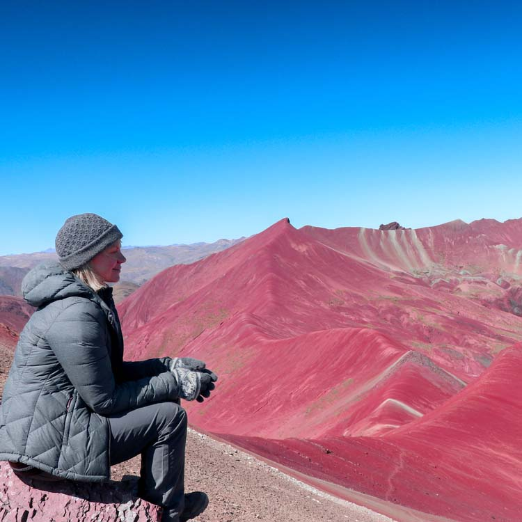 A traveler in a winter jacket and gloves sitting on a rocky ridge.