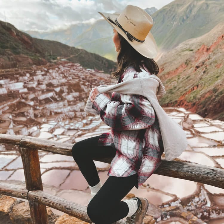 A traveler in a wide-brimmed hat and layered clothing sitting on a wooden fence.