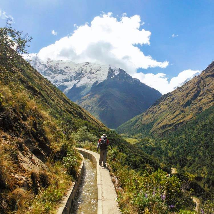 how long acclimate cusco peru humantay lake trail A lone hiker with a red backpack walking along a narrow trail through a lush green valley.