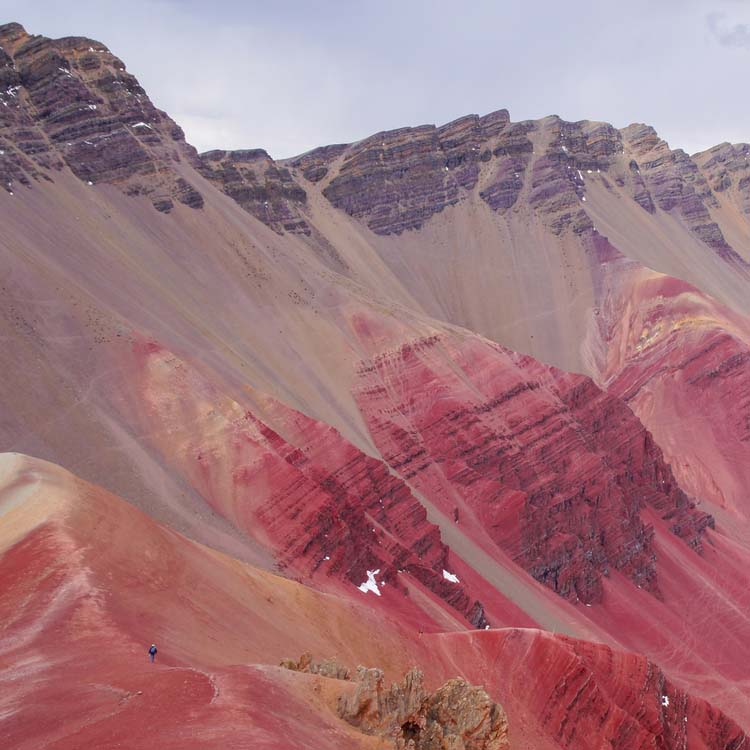 A lone hiker dwarfed by the dramatic red and purple mineral layers of Red Valley.