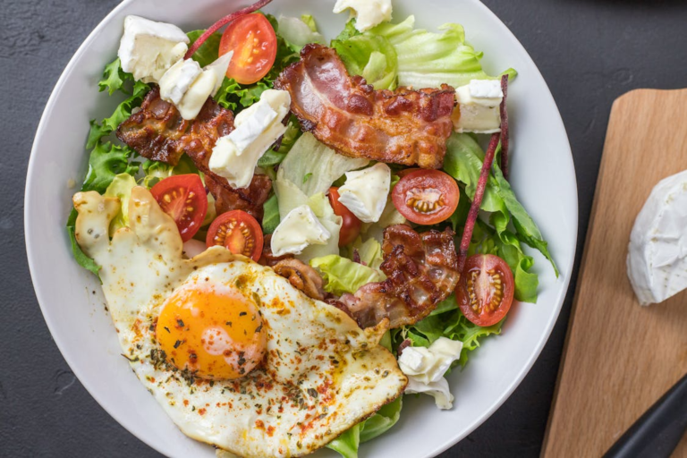 A bowl of fresh salad with a fried egg, bacon, cherry tomatoes and goat cheese.
